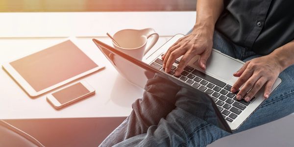 Male sitting on bench with laptop, coffee, tablet, and cell phone