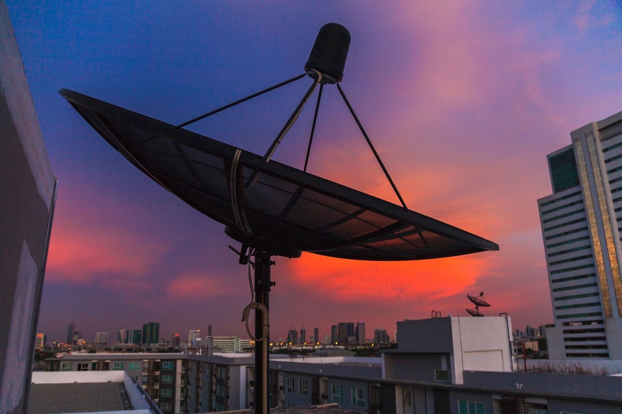 Satellite dish on a rooftop during sunset.