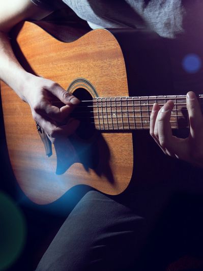 Close-up of hands playing an acoustic guitar in moody lighting.