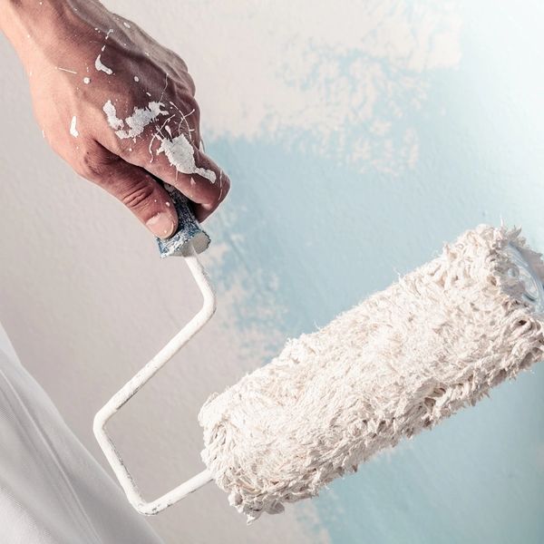 Hand holding paint roller with white paint.