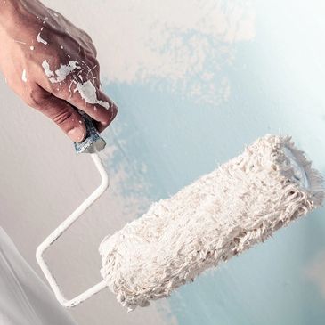 hand holding a paint roller covered in white paint