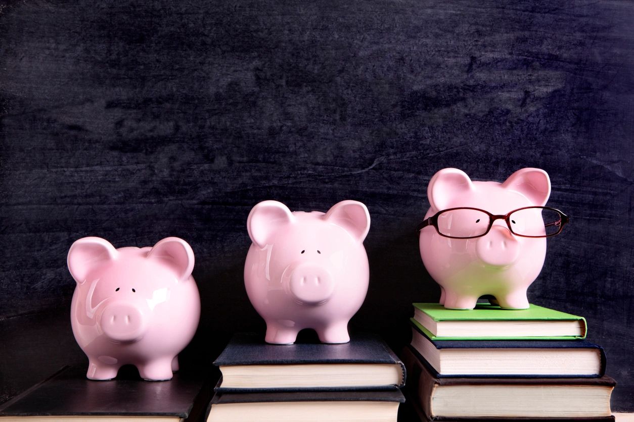 Three piggy banks standing on books.