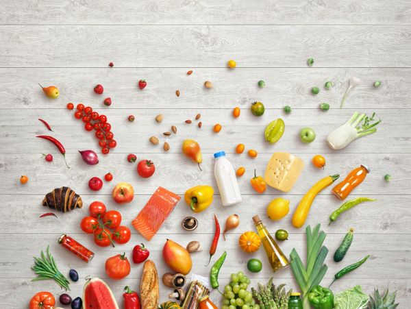 A colorful assortment of fresh fruits, vegetables, and groceries on a light wooden surface.