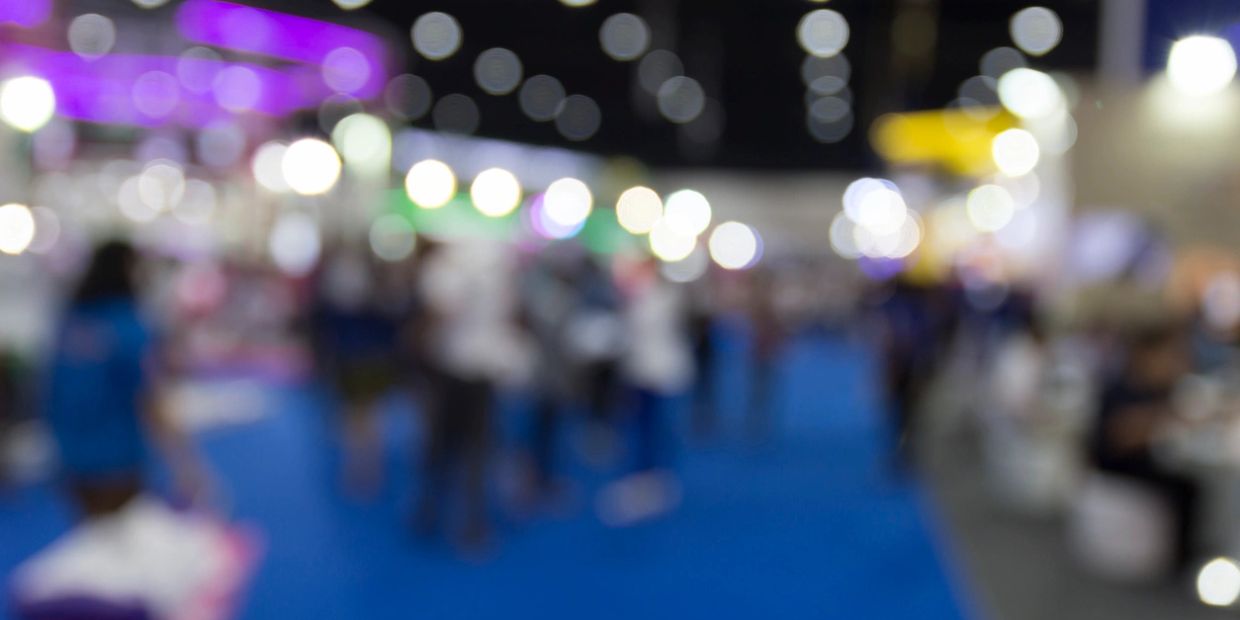 Blurred image of people at a brightly lit indoor event with colorful lights.