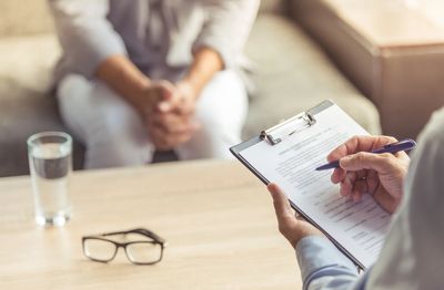 Client, counselor talking, taking notes, a glass of water on the table, eyeglasses, hands clasped