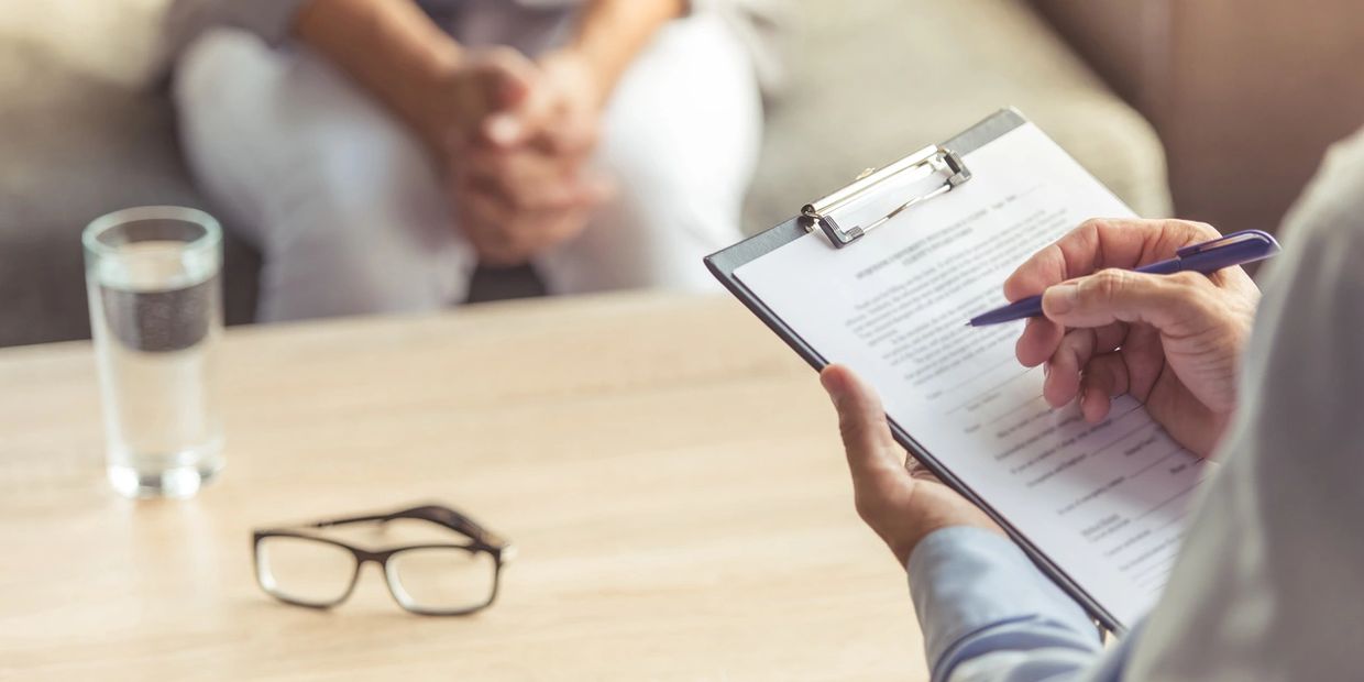 Person holding a pen and clipboard during a consultation with another person.