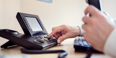 Person dialing a number on a desk phone.