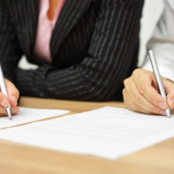 Two people signing documents with silver pens at a wooden table.