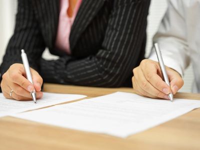 Two professionals signing documents at a desk.
