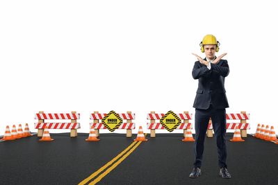 Man in suit and helmet signaling stop near a construction zone.