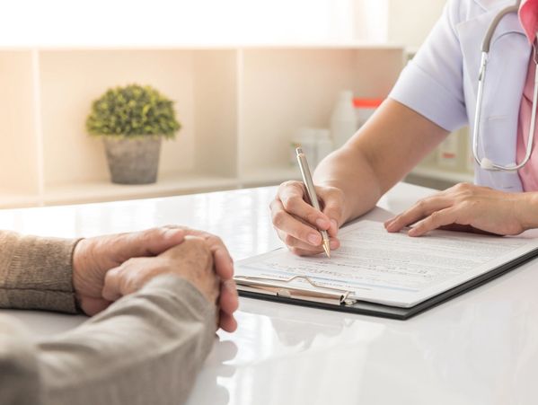 Doctor filling out medical forms while patient listens.