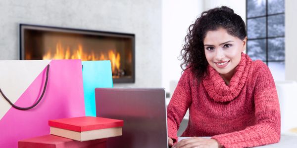 Woman smiling in front of computer, fireplace, gift boxes in winter in front of window with snow outside. 