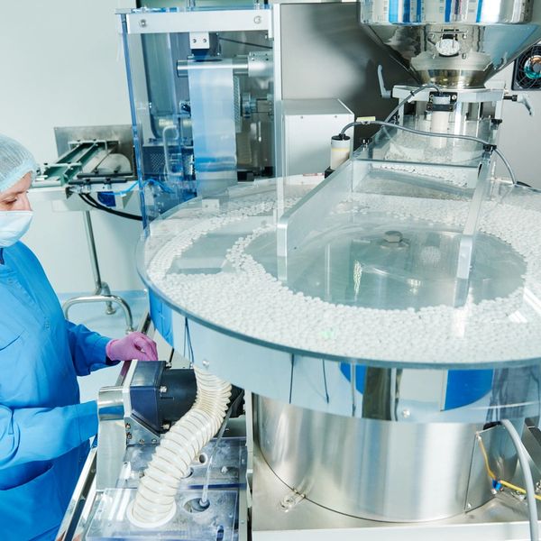 Worker in protective gear monitoring pill production in a pharmaceutical factory.