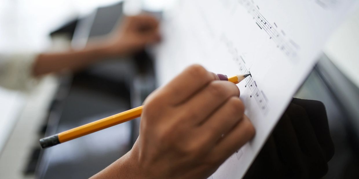 A person writing music notes on a sheet with a pencil.