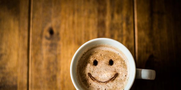A cup of coffee with a smiley face drawn in the foam on a wooden table.