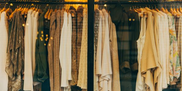 Closet with various beige and brown coats and sweaters on hangers.