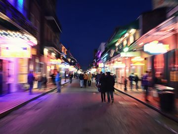 A blurry nighttime street scene with colorful lights and people walking.