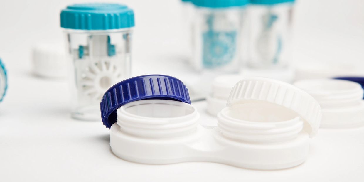 Open contact lens case with blue and white caps on a white surface.