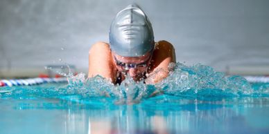 Swimmer in silver cap performing breaststroke in a pool.