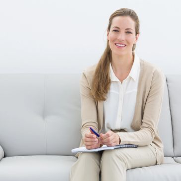 Smiling woman with notebook and pen sitting on a sofa.