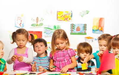 A group of young children painting and drawing together in a classroom.