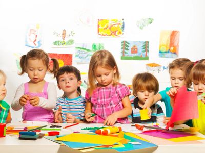 Children engaged in arts and crafts at a colorful classroom table.