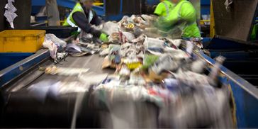 Workers sorting recyclable materials on a conveyor belt at a recycling facility.