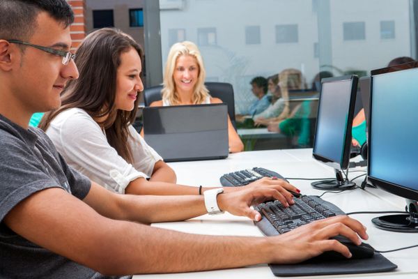 Young adults collaborating on computers in a modern office setting.