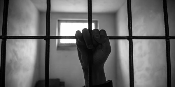 A gripping image of a hand tightly grasping the bars of a darkened jail cell representing contrast.