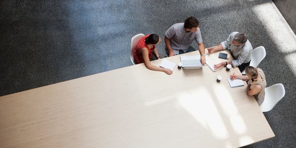 Overhead image of four people sitting at the end of a long  table. Working on a project together. 