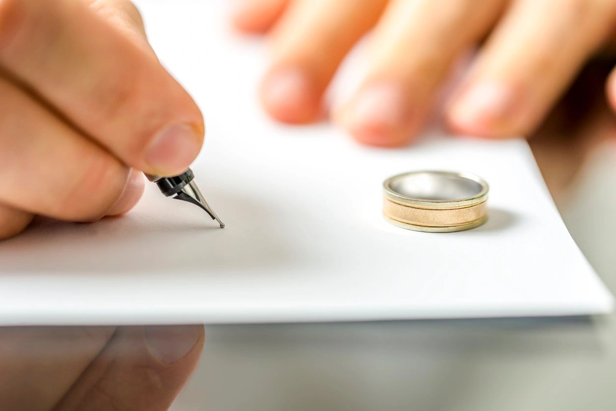 Signing divorce documents beside wedding rings.