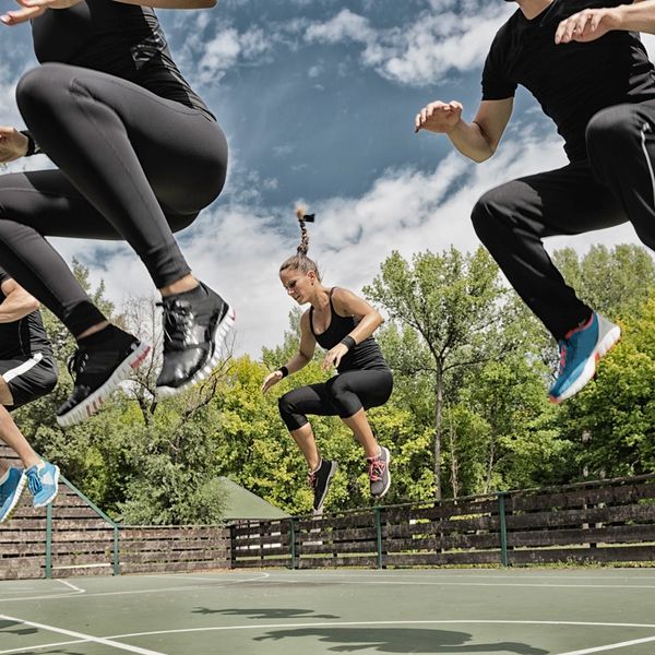 Group fitness class jumping outdoors on a sunny day.