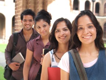 Four students smiling outdoors with books and backpacks.