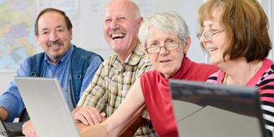 A group of elderly people happily using laptops together.