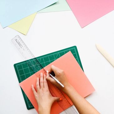 hands using a ruler over colored paper to begin a design