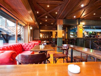 Cozy pub interior with wooden ceiling, red sofa, and wooden tables and chairs.