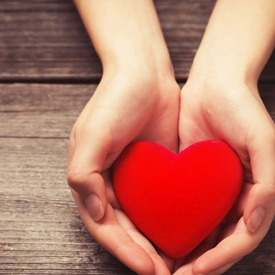 Hands gently holding a red heart on a wooden surface, representing a safe space to feel heard and held.