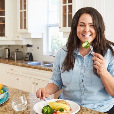 Smiling woman in her 30's in kitchen eating healthy food
