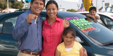 Happy family holding car keys in front of a new car for sale.