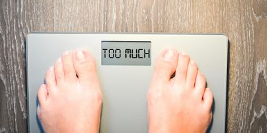 Feet on a scale displaying the words 'TOO MUCH'.