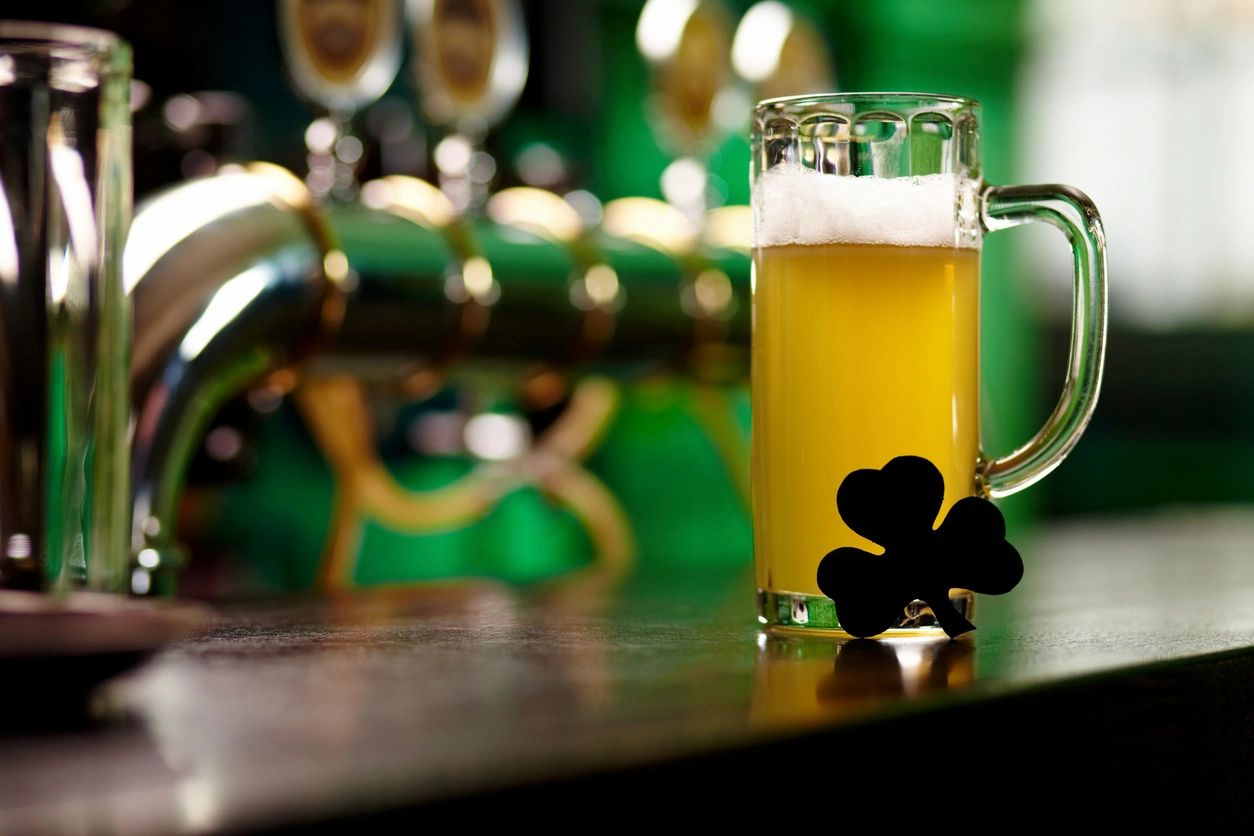 A beer mug with a shamrock on a bar counter, with beer taps in the background.