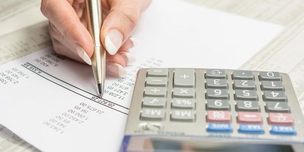 Person using a pen and calculator to work on financial documents.