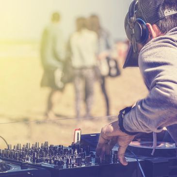 DJ mixing music at an outdoor beach party with friends in the background.