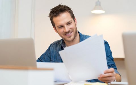 Man in a blue shirt smiling and looking at paperwork