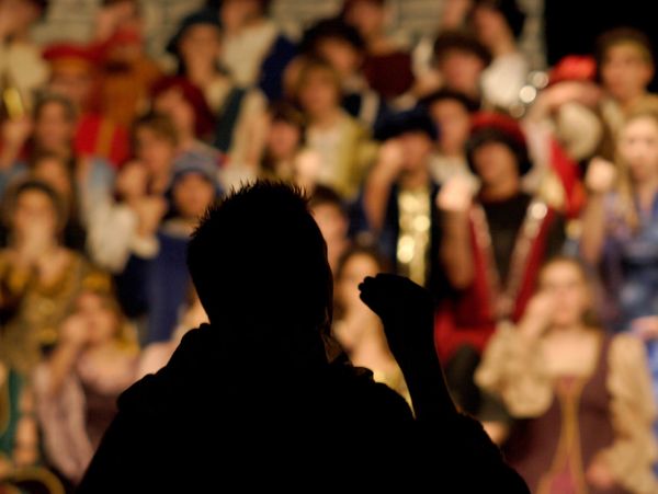Silhouette of a person addressing a blurred audience in colorful attire.