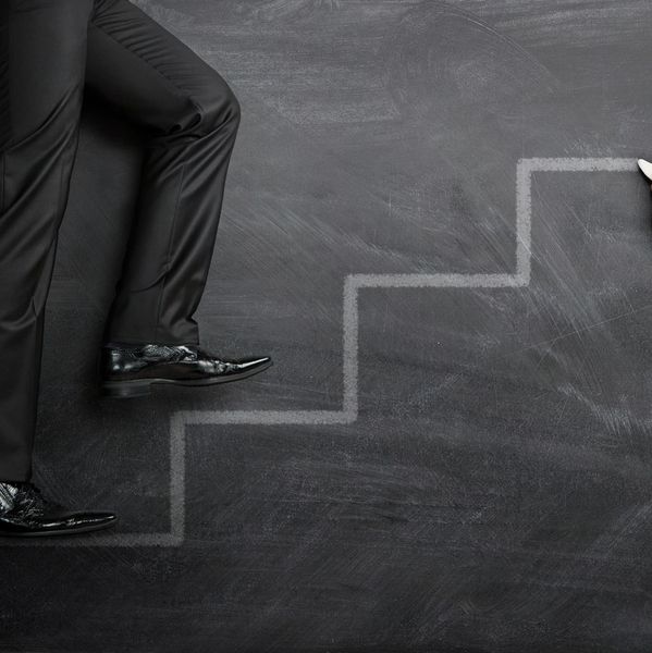 Person climbing chalk-drawn stairs on a blackboard, symbolizing progress.