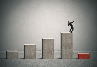 Four blocks increasing in size.  A man is standing on the final tallest block losing his balance.