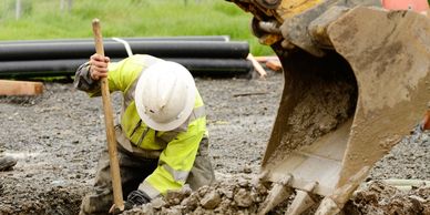 Contractor digging with shovel in front of excavator for French drain