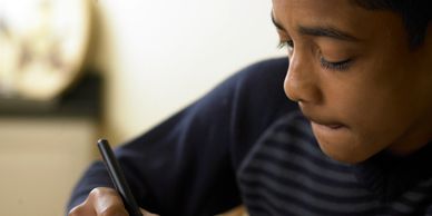 Young boy concentrating while writing with a pen.