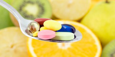 Colorful vitamin pills on a spoon with fresh fruits background.